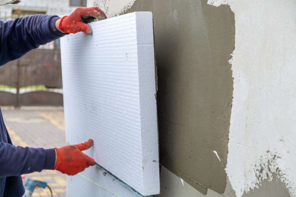Handwerker befestigt Dämmstoffplatte an der Außenfassade zur Fassadendämmung