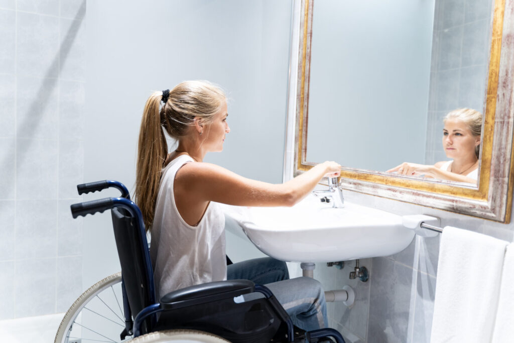 Frau im Rollstuhl benutzt Waschbecken in barrierefreiem Badezimmer